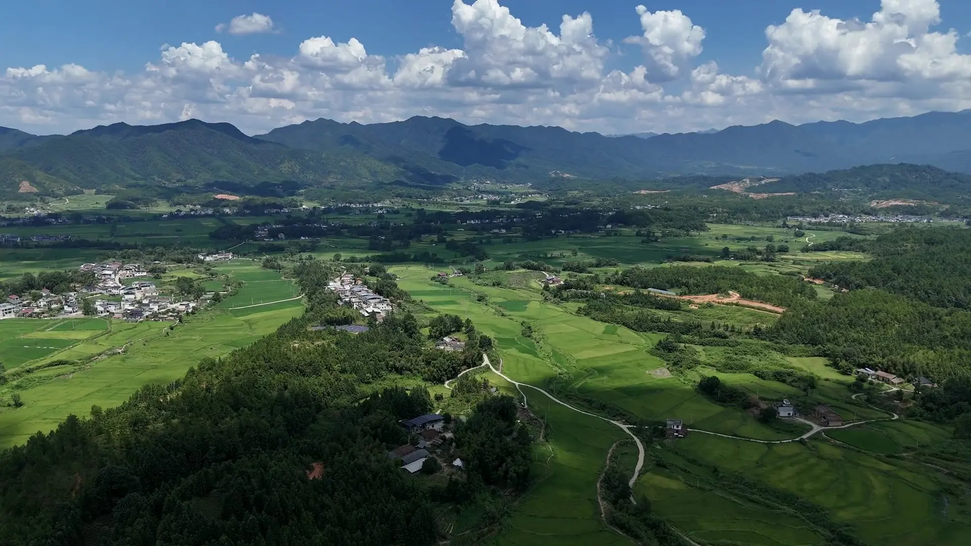 Vista aérea de um vale verde entre morros, com lavouras, mata e um pequeno povoado