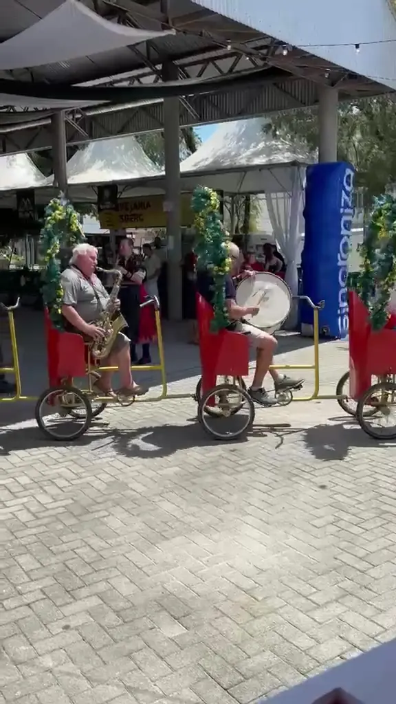 Músicos com trajes típicos em triciclos enfeitados tocam bumbo e saxofone na praça do festival